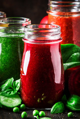 Multicolored vegan vegetable juices and smoothies from tomato, carrot, pepper, cabbage, spinach, beetroot in glass bottles on rustic kitchen table, vegetarian food and drink concept, selective focus