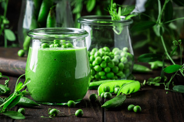 Cream soup from green peas in glass jar on brown wooden kitchen table background, vegan food concept, copy space, selective focus