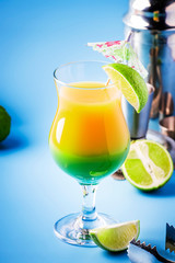 Double layer green yellow alcoholic cocktail with mango juice, rum, liqueur, lime and ice, blue background, copy cpase