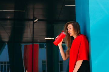 girl in red leather jacket drinks from red thermal mug near a mo