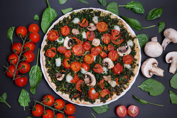 Pizza vegana con espinacas, tomates cherry y champiñones sobre fondo negro.