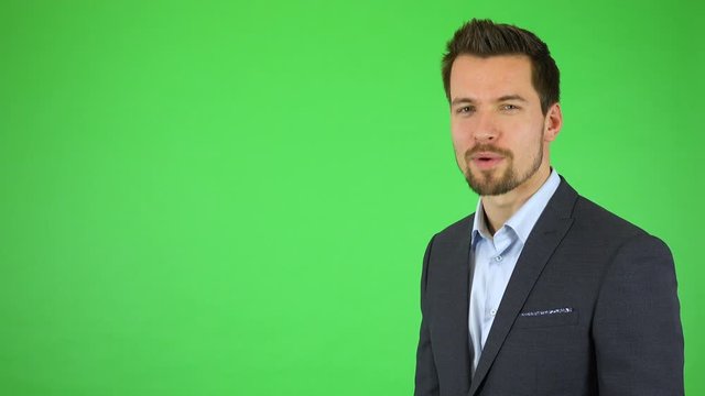 A young handsome businessman talks to the camera, pointing at bullet-point texts sliding toward him - green screen studio