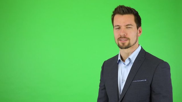 A young handsome businessman talks to the camera and drags bullet-point text toward him with his fingers - green screen studio