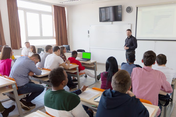 Male professor explain lesson to students and interact with them in the classroom.Helping a students during class.