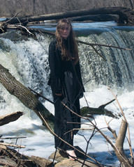 Young  tall Woman with dark long hair in black robes in front of the Waterfall. Witches. Halloween concept. Witchcraft and magic. 