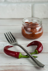 harissa in a glass jar with a fork and fresh red chili peppers on white background