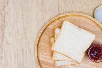 Top view of sliced bread and strawberry jam on wooden background closeup, soft warming tone.