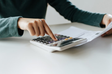 young woman using calculator for analysis and calculating family budget cost bills report on desk in home office, plan money cost saving, investment, business finance, expenses and income concept