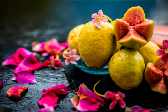 Raw organic guava or amrut or amarood in Hindi language on black shinny surface in a blue-colored plate with some rose petals.