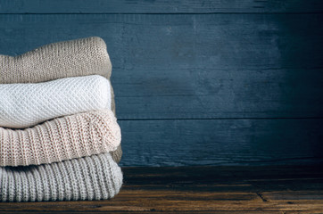 Pile stack folded of knitted warm sweaters clothes on wooden background, sweaters, knitwear, copy space for text.