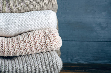 Fototapeta na wymiar Pile stack folded of knitted warm sweaters clothes on wooden background, sweaters, knitwear, copy space for text.