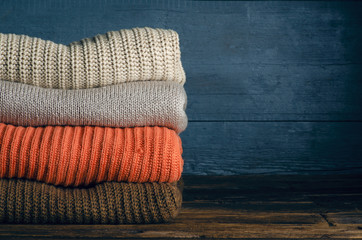 Pile stack folded of knitted warm sweaters clothes on wooden background, sweaters, knitwear, copy space for text.