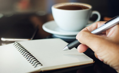 Closeup of hand businessman working and writing on notbook with smartphone and drink coffee in cafe