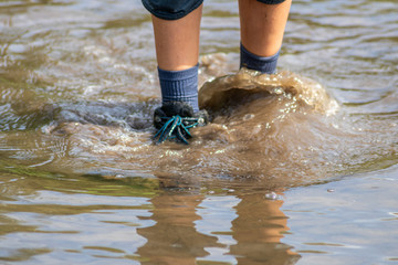 Junge watet mit nassen Schuhen und nassen Socken durch Hochwasser nach einer Überschwemmung mit starkem Regen und Deichbruch