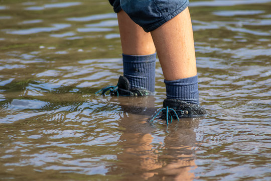 Junge watet mit nassen Schuhen und nassen Socken durch Hochwasser nach einer &Uuml;berschwemmung mit starkem Regen und Deichbruch