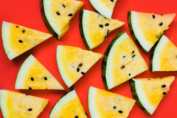 a lots of triangular pieces of ripe yellow watermelon on red background