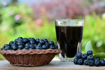 Black chokeberry berries in a basket and a glass of drink on a wooden table on the background of the garden close-up