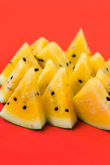 a lots of triangular pieces of ripe yellow watermelon on red background