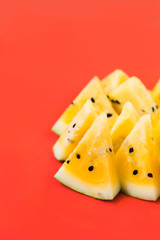 a lots of triangular pieces of ripe yellow watermelon on red background