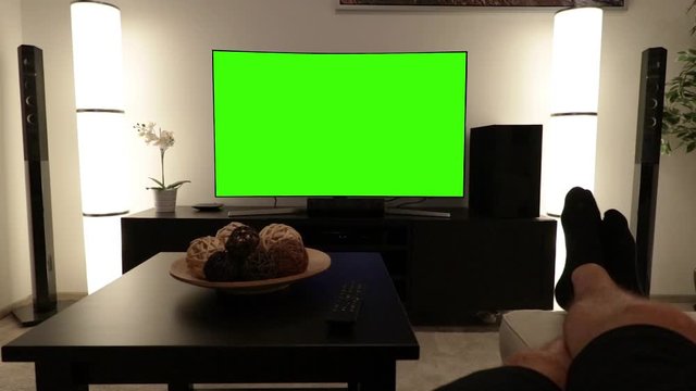 POV man lies on a couch in an apartment living room and watches TV with green screen