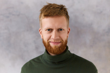 Fototapeta premium Cheerful handsome young man with stylish hairdo, neat trimmed beard and blue eyes expressing positive emotions, smiling at camera. People, masculinity, men's wear, style, fashion and grooming concept