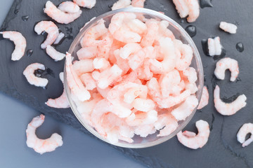 Frozen raw peeled shrimps in a glass bowl on a dark background, horizontal, top view