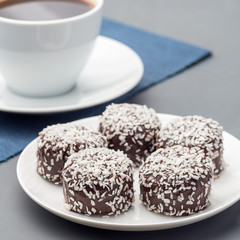 Swedish sweets chocolate balls or chokladbollar, made from oats, cocoa, butter and coconut, on a white plate, served with coffee,  square