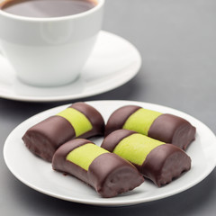 Swedish sweets punch rolls or punschrullar, covered with green marzipan, on a white plate, served with coffee, square format