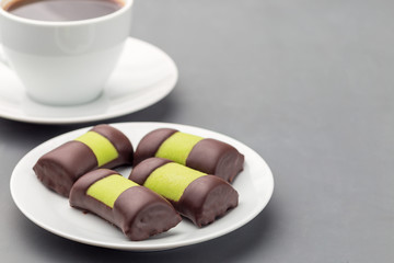 Swedish sweets punch rolls or punschrullar, covered with green marzipan, on a white plate, served with coffee, horizontal, copy space