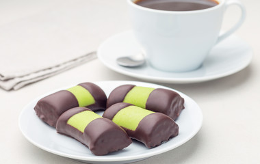 Swedish sweets punch rolls or punschrullar, covered with green marzipan, on a white plate, served with coffee, horizontal