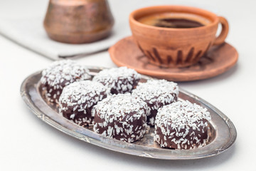 Swedish sweets chocolate balls or chokladbollar, made from oats, cocoa, butter and coconut, on a metal plate, served with coffee, horizontal