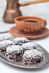 Swedish sweets chocolate balls or chokladbollar, made from oats, cocoa, butter and coconut, on a metal plate, served with coffee, vertical