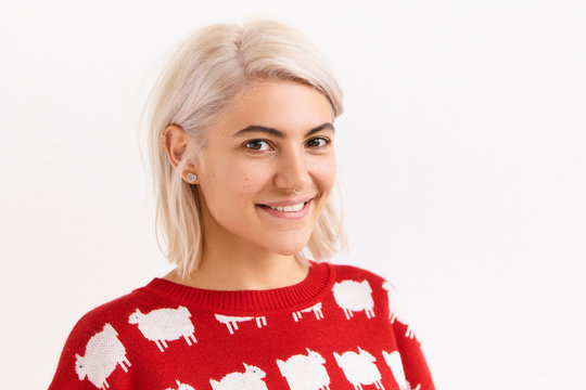 Horizontal image of beautiful European student girl rejoicing at good positive news, gets A mark, posing isolated in red sweater, looking at camera with cute adorable smile, showing straight teeth