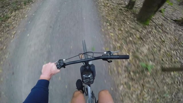 POV man rides a bicycle down a narrow road through a forest, pulls out a water bottle and drinks