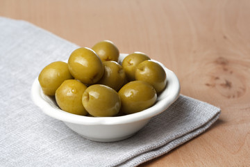 green pitted olives in a small white plate on a wooden table surface