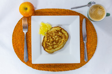 Delicious dietary breakfast of a pancake with pineapple, an apple, coffee, served on a square white plate and a wicker placemat, flat lay, top view, color and texture