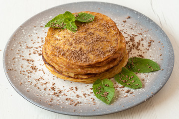 Stack of American pancakes with some mint and chocolate leaves in a gray plate on a wooden table. cooking concept.