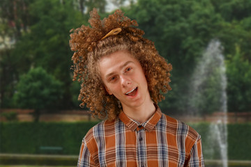 Portrait of a curly-haired young man with a wooden comb in full hair smiling in a park background. male hair care concept