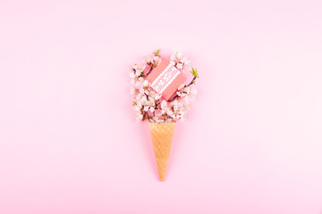Ice cream waffle cone with colorful flowers and gift box on pink background. Flat lay. Minimal gift birthday concept