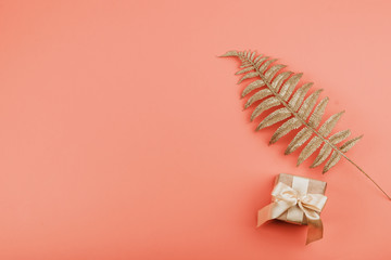 Gift box with bow and Golden palm leaves on coral background. Festive minimal background