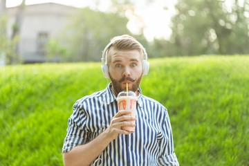 Fototapeta premium Handsome relaxed young hipster man with a mustache and beard is listening to favorite music at the earphones while walking through the park. Music subscription concept and online radio.