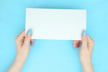 Obraz premium White sheet of paper in the hands of a caucasian girl. Manicure on the nails. Turquoise background.