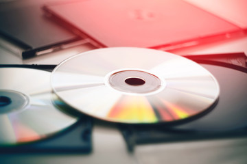 Two disks lie in black plastic packages for disks and gleam in different colors, illuminated by a bright red light.