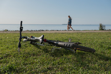 Fototapeta na wymiar Report from the seashore. The bicycle lies on a green grass. People walk along the water. Summer. Sunny day.