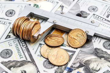 Vernier caliper with coins on background of dollar bills. Business concept.