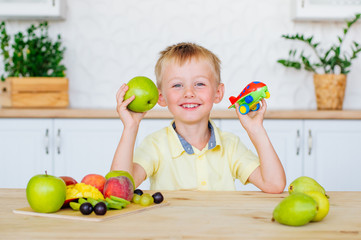 Fototapeta premium Happy little boy eating green apples in the kitchen