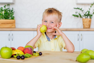 Fototapeta premium Happy little boy eating fresh pear in the kitchen