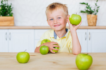 Happy little boy eating green apples in the kitchen