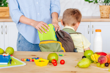 Mother putting lunch box into her sons backpack