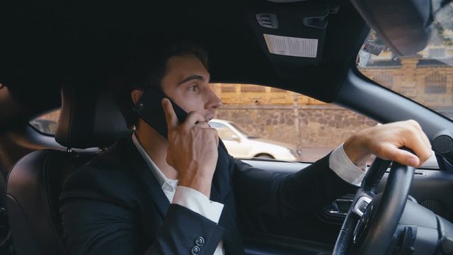 Busy Businessman Driving a Car and talking on Mobile Phone. Portrait of a Young Confident Man is Driving Car and using Smartphone in a City.